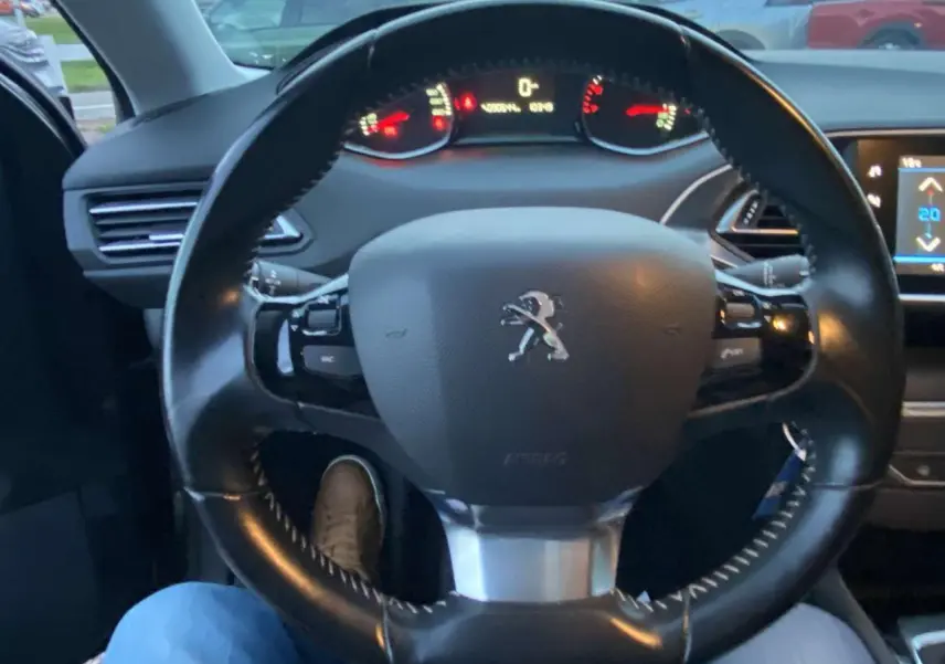 Vue intérieure centrée sur le volant cuir noir du Peugeot 308 2020 avec tableau de bord et écran tactile visible.