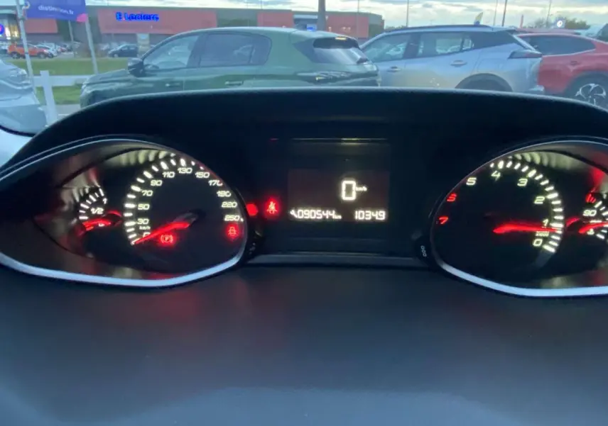 Vue du tableau de bord éclairé d'une Peugeot 308 gris clair, affichant le compteur de vitesse et le compte-tours.