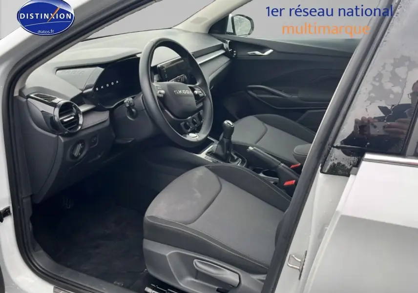 Intérieur côté conducteur d'une Skoda Fabia blanche 2025, montrant sièges noirs et tableau de bord moderne.