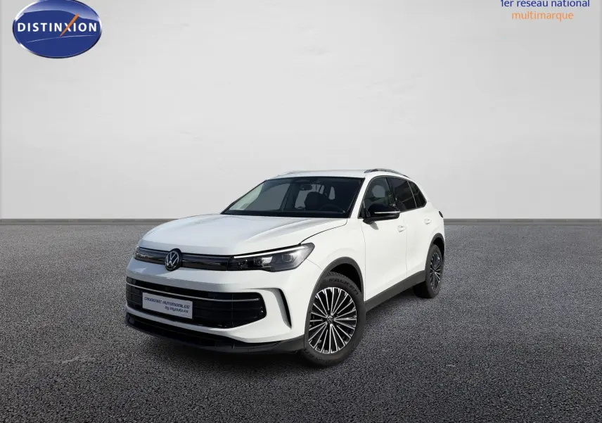 Volkswagen Tiguan blanc en 3/4 avant droit, avec jantes alliage noir brillant, devant un concessionnaire.