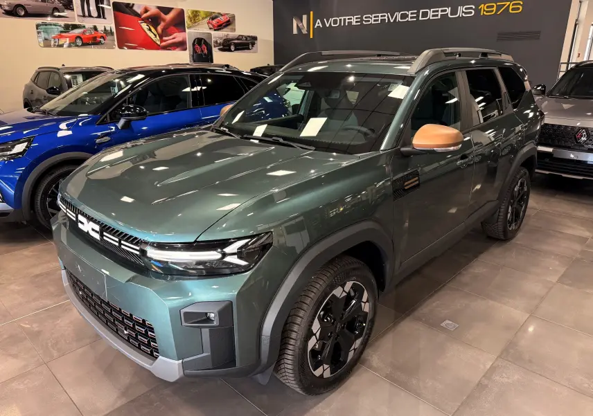 Vue 3/4 avant droite du Dacia Bigster Hybrid-G 150 4x4 en Vert Cèdre avec rétroviseurs couleur beige dans un showroom.