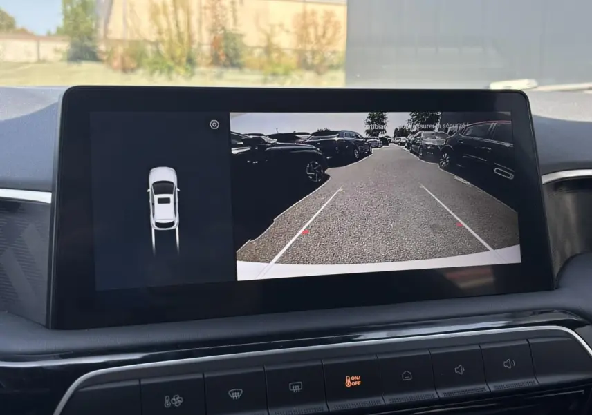 Écran central tactile montrant la caméra de recul du MG3 blanc Dover, avec vue arrière sur un parking extérieur.