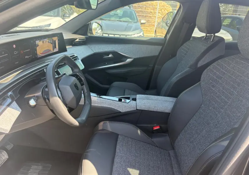 Vue intérieure côté conducteur du Peugeot 3008 Hybrid 145 e-DCS6 Allure 2025, sièges tissu gris et cuir noir, tableau de bord numérique.