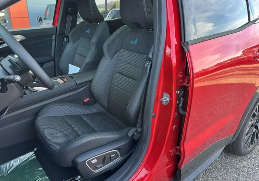 Vue intérieure côté conducteur du Renault Austral 2025 rouge toit noir, sièges sport avec logo Alpine bleu sur appuie-tête.