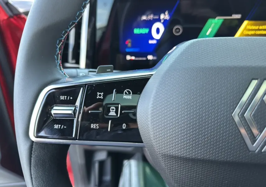 Gros plan sur le volant du Renault Austral 2025 rouge toit noir, avec commandes intégrées et tableau de bord numérique lumineux.