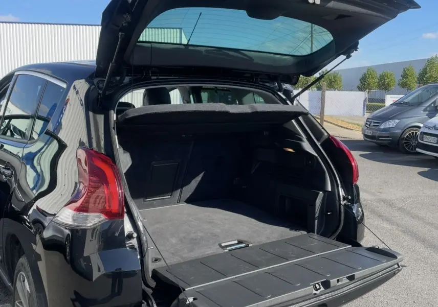 Peugeot 3008 noir vue 3/4 arrière gauche avec coffre ouvert et hayon à double ouverture sous un ciel bleu.