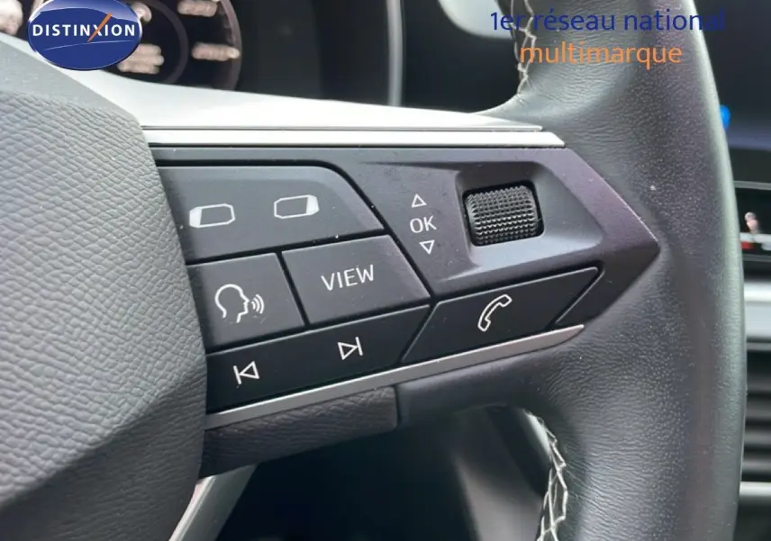 Gros plan sur les commandes au volant en cuir noir du SEAT LEON ST gris urbain, mettant en valeur les boutons multifonctions.