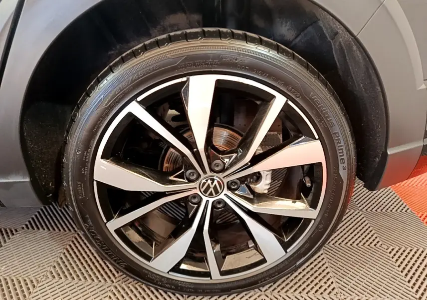 Gros plan sur la roue avant droite du Volkswagen Taigo noir, avec jante alliage bicolore et logo VW au centre.