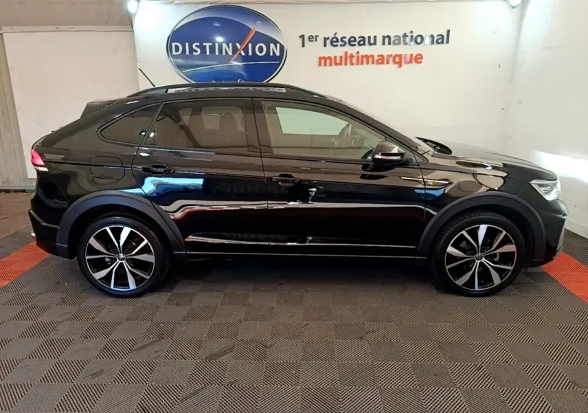 Profil droit d'un Volkswagen Taigo noir 2023 R-Line avec jantes alliage et toit ouvrant en intérieur showroom.