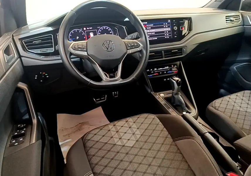 Vue intérieure avant du Volkswagen Taigo 1.5 TSI 150 DSG R-Line avec volant cuir, tableau de bord digital et sièges tissu à motifs.