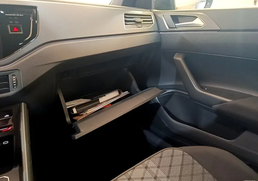 Intérieur côté passager du Volkswagen Taigo noir 2023, boîte à gants ouverte avec documents visibles.