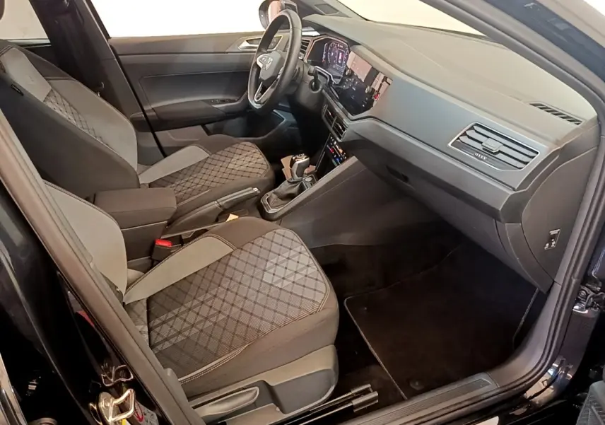 Vue intérieure côté passager avant du Volkswagen Taigo noir 2023, sièges tissu à motifs et tableau de bord moderne.