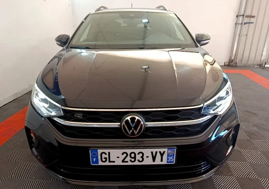 Vue frontale d’un Volkswagen Taigo 1.5 TSI R-Line noir avec phares LED et calandre chromée en intérieur showroom.