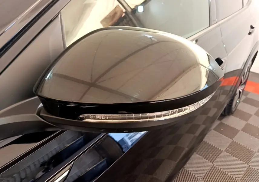 Gros plan sur le rétroviseur droit noir brillant du Volkswagen Taigo 1.5 TSI 150 DSG R-Line avec clignotant intégré.