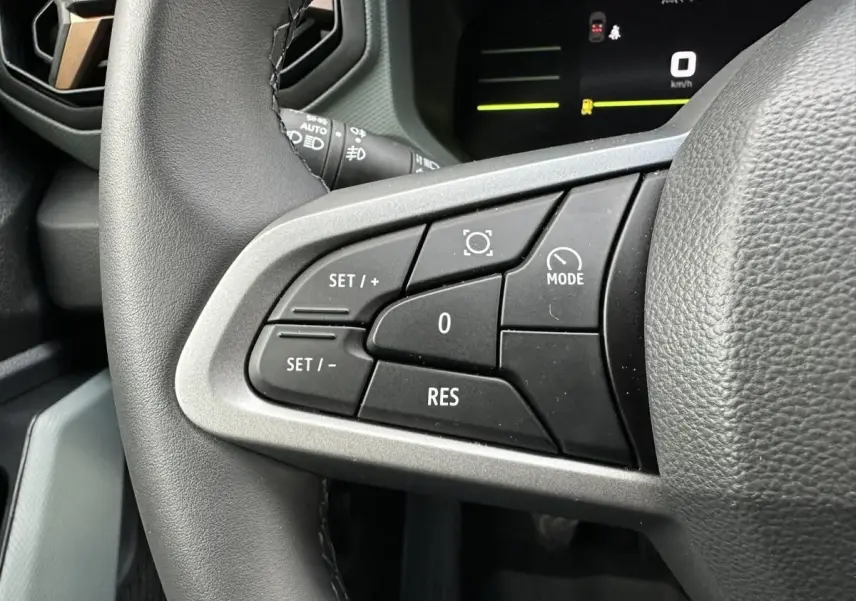 Gros plan sur les commandes au volant à gauche du Dacia Duster blanc Glacier 2025, avec affichage numérique en arrière-plan.