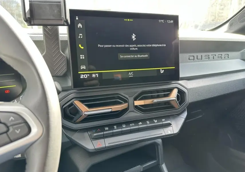 Tableau de bord du Dacia Duster 2025 avec écran tactile, aérateurs hexagonaux et inscription DUSTER côté passager.