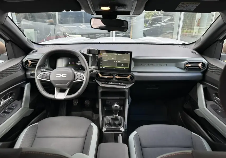 Vue intérieure avant du Dacia Duster blanc glacier 2025, tableau de bord moderne avec écran tactile central et volant multifonction.