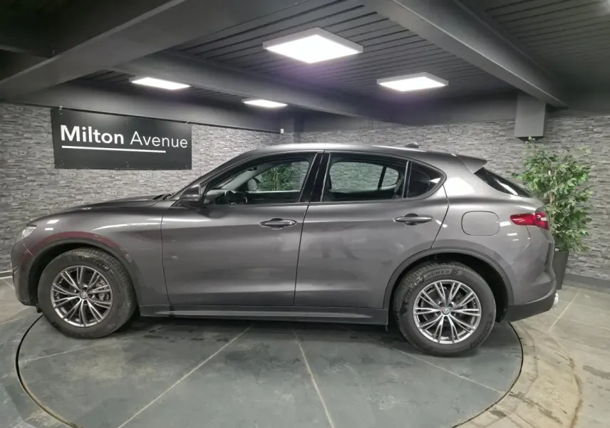 Vue de profil côté gauche d'un Alfa Romeo Stelvio gris métallisé avec jantes alliage 18 pouces dans un showroom.
