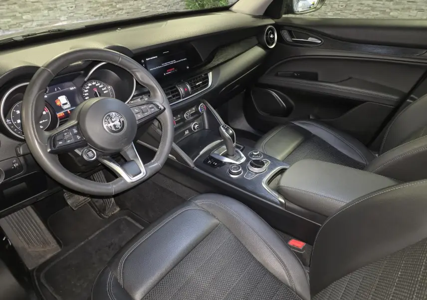 Vue intérieure côté conducteur de l'Alfa Romeo Stelvio 2022, avec volant cuir sport et tableau de bord noir.