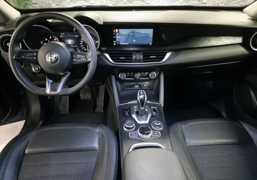 Vue intérieure frontale de l'Alfa Romeo Stelvio 2022, tableau de bord noir avec écran tactile et volant cuir sport.