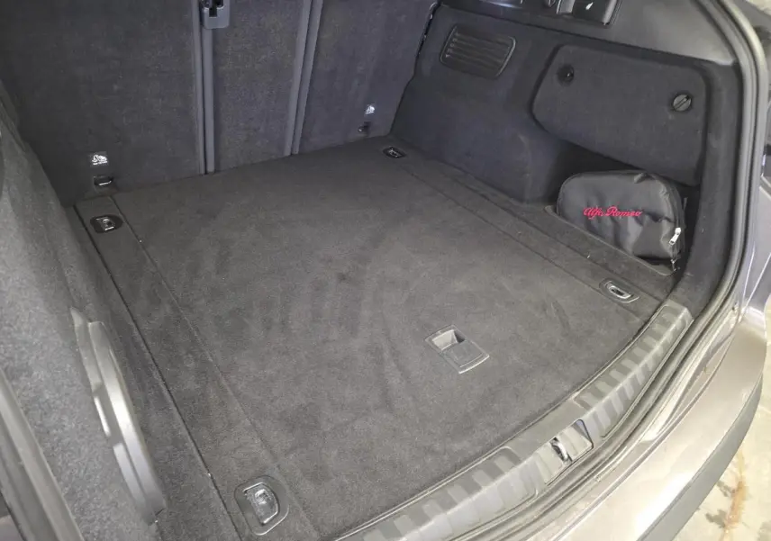 Coffre spacieux de l'Alfa Romeo Stelvio gris, vue arrière avec tapis noir et trousse de secours brodée Alfa Romeo.
