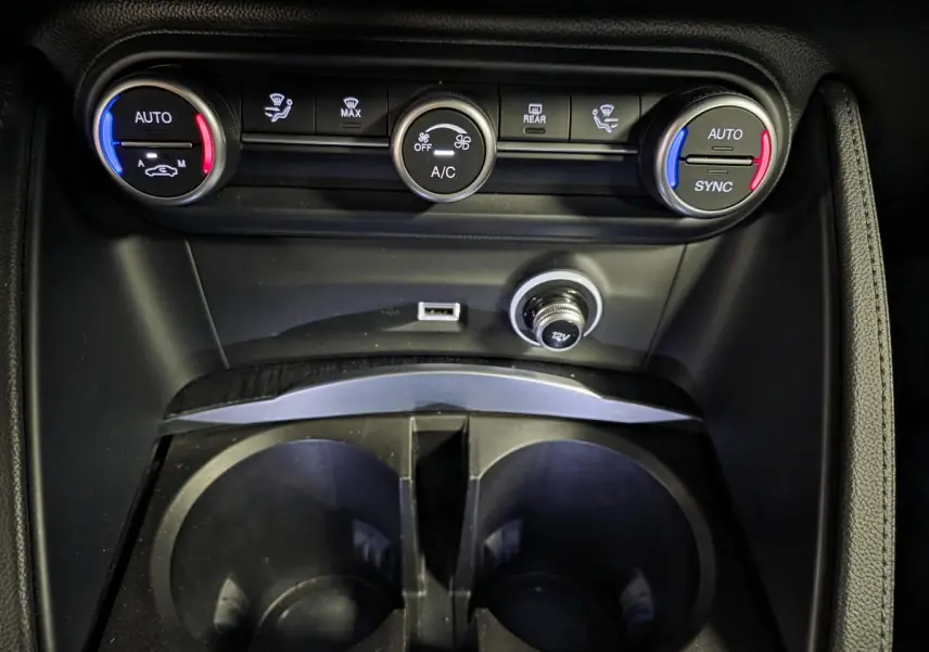 Vue rapprochée de la console centrale de l'Alfa Romeo Stelvio 2022, avec commandes climatisation bi-zone et prises USB/12V.