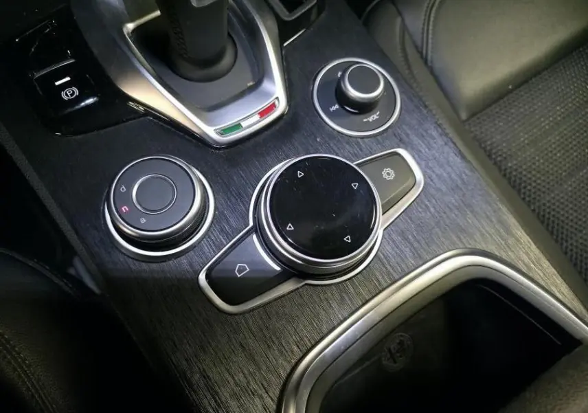 Gros plan sur la console centrale en finition bois foncé de l'Alfa Romeo Stelvio avec commandes rotatives et levier de vitesse.