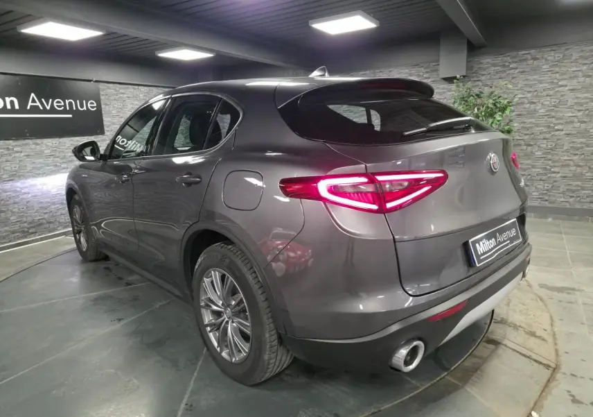 Vue 3/4 arrière droite d'un Alfa Romeo Stelvio gris métallisé avec feux arrière LED et double sortie d'échappement.