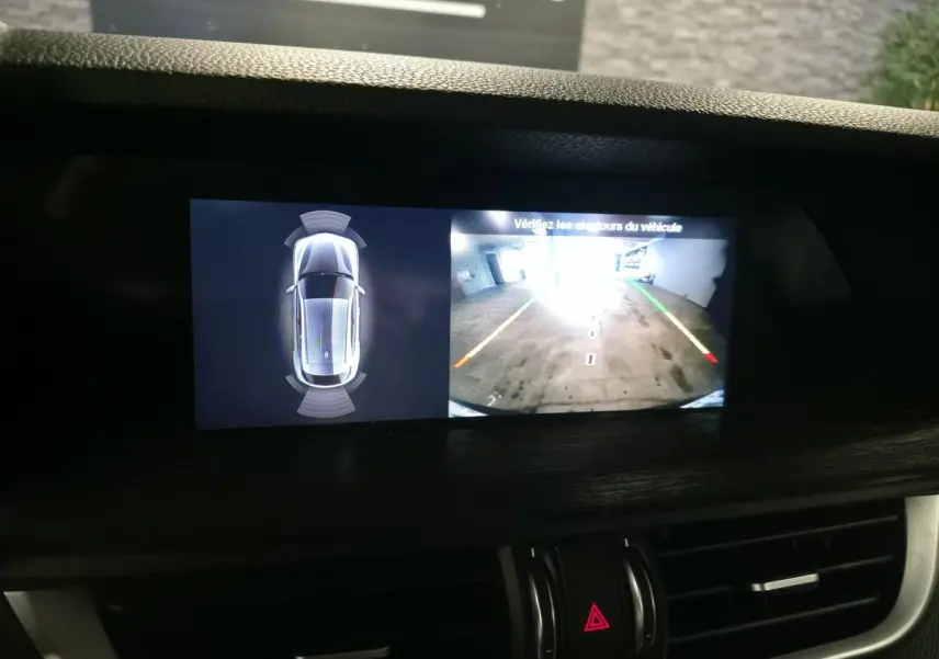 Écran central de l'Alfa Romeo Stelvio gris montrant la caméra de recul et l'alerte de proximité en intérieur.