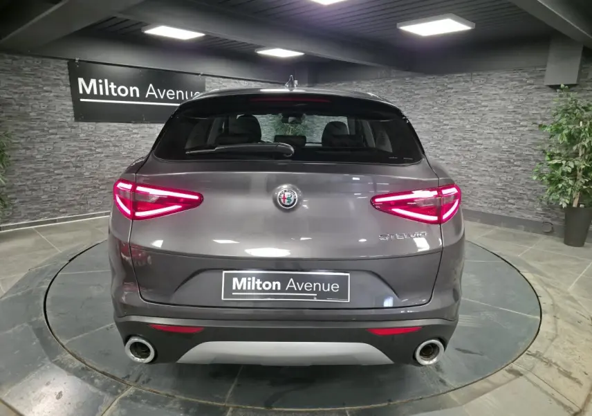 Vue arrière d'un Alfa Romeo Stelvio gris métallisé avec feux LED allumés et double sortie d'échappement.