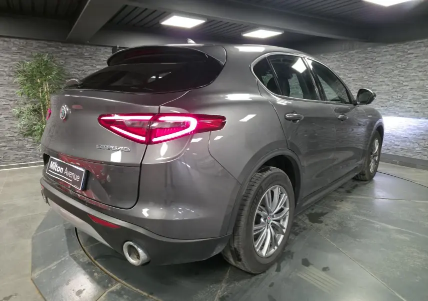Vue 3/4 arrière droite d'un Alfa Romeo Stelvio gris métallisé avec feux arrière LED et jantes alliage 18 pouces.