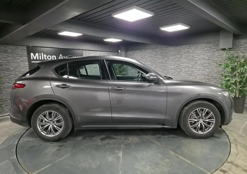 Profil droit d'un Alfa Romeo Stelvio gris métallisé 2022 avec jantes alliage 18 pouces Luxury en intérieur showroom.
