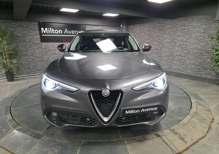 Vue frontale d'une Alfa Romeo Stelvio gris métallisé avec phares LED allumés dans un showroom.