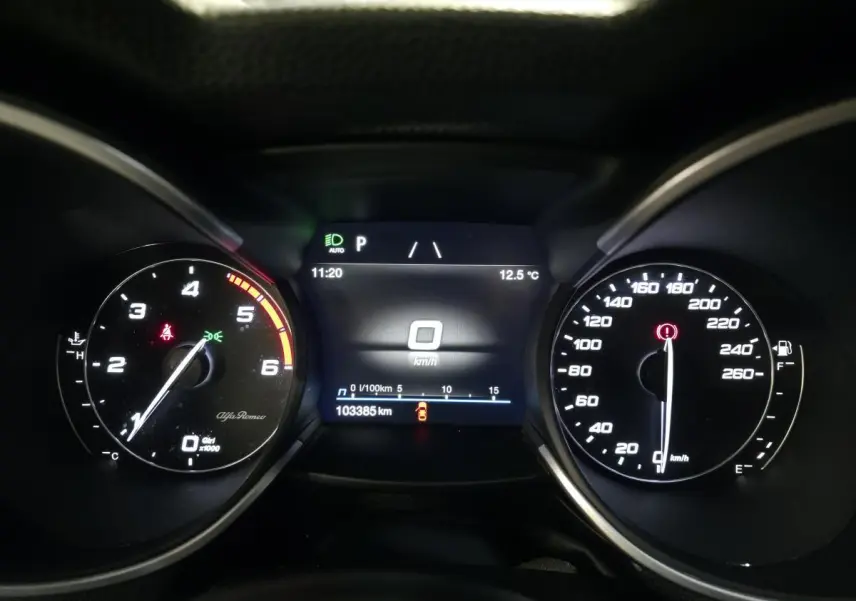 Vue rapprochée du tableau de bord numérique de l'Alfa Romeo Stelvio gris, affichant la vitesse à 0 km/h et 103385 km au compteur.