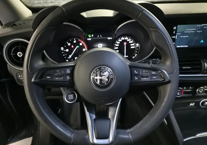 Vue rapprochée du volant cuir noir d'Alfa Romeo Stelvio 2022 avec commandes intégrées et tableau de bord numérique.