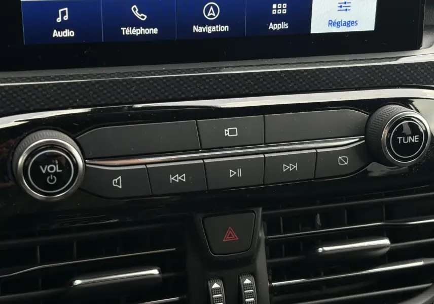 Vue rapprochée de la console centrale du Ford Kuga 2023, boutons audio noirs avec écran tactile visible en haut.