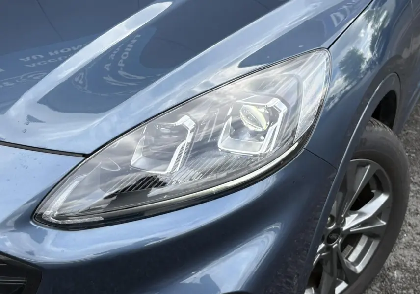 Gros plan sur le phare avant droit et la roue alliage 18 pouces d'un Ford Kuga 2.0 EcoBlue bleu azur 2023.