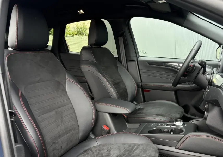 Vue intérieure côté droit du Ford Kuga ST-Line X 2023, sièges noirs avec surpiqûres rouges et volant méplat.