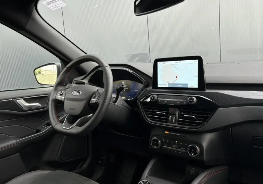 Vue intérieure côté conducteur du Ford Kuga 2023, volant ST-Line avec surpiqûres rouges et écran tactile GPS central.