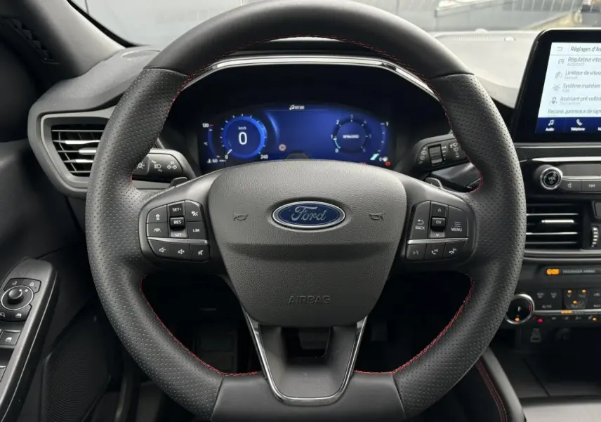 Vue frontale du volant perforé noir avec surpiqûres rouges du Ford Kuga 2023, tableau de bord numérique et écran tactile visibles.