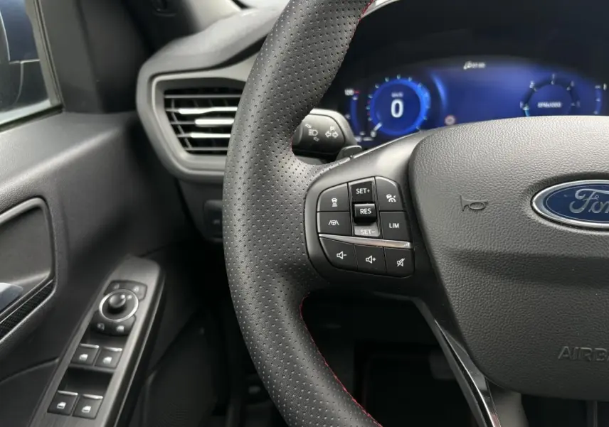 Vue rapprochée du volant perforé avec surpiqûres rouges et tableau de bord numérique bleu du Ford Kuga 2023.
