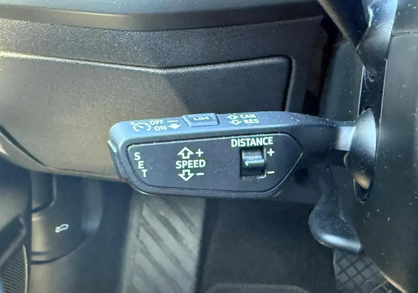 Gros plan sur la commande de régulateur de vitesse adaptatif à gauche du volant de l'Audi A3 Sportback blanc Arkona 2024.