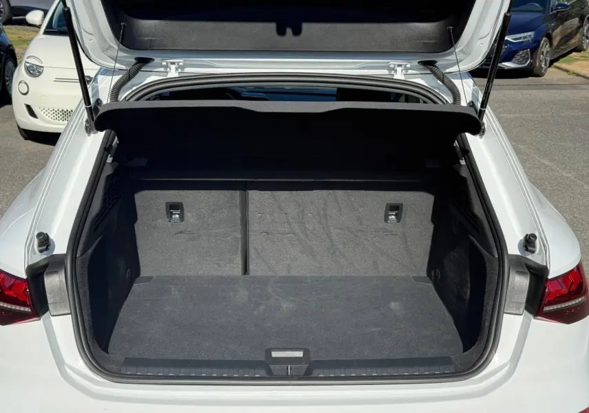 Coffre ouvert vu de l'arrière d'une Audi A3 Sportback blanche Arkona 2024, intérieur noir et spacieux.