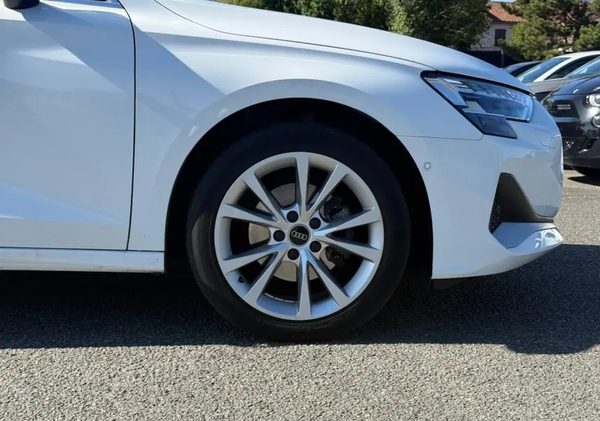 Gros plan sur la roue avant gauche et le pare-chocs avant blanc Arkona d'une Audi A3 Sportback 2024.