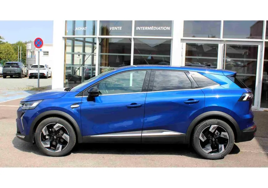 Profil droit d'un Renault SYMBIOZ bleu 2025 avec jantes alliage noires et détails chromés, stationné devant un bâtiment vitré.
