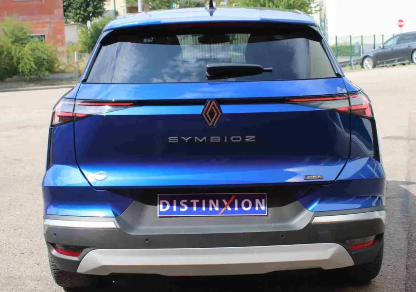 Vue arrière d’un Renault SYMBIOZ bleu avec feux LED fins et logo central, sur un parking extérieur.