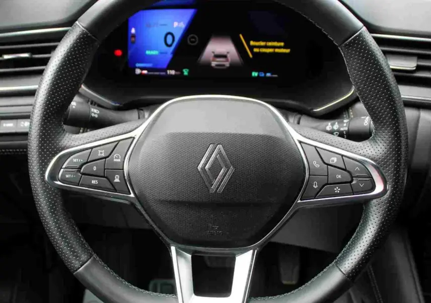 Vue rapprochée du volant noir perforé avec logo Renault et tableau de bord numérique du Renault Symbioz 2025.