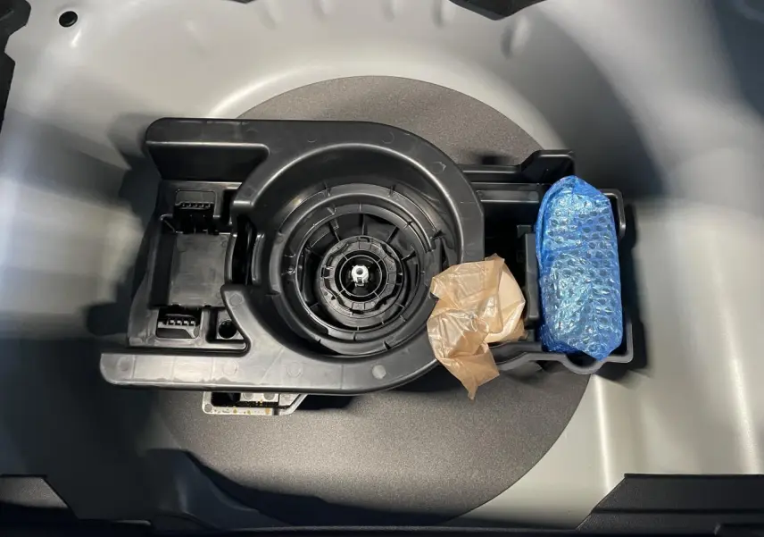 Vue plongeante sur le kit de dépannage pneumatique noir dans le coffre gris clair de la Peugeot 208 blanc okenite.