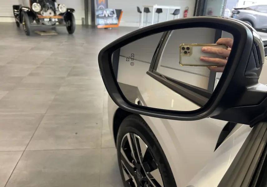 Rétroviseur droit d’une Peugeot 208 blanche Okenite, avec jante alliage 16’’ et reflet intérieur visible.