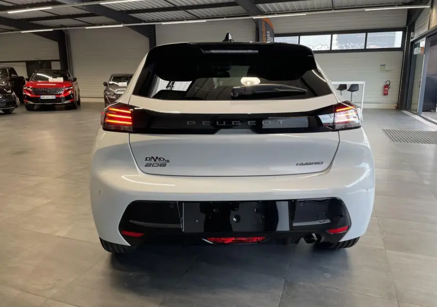 Vue arrière d'une Peugeot 208 hybride blanche Okenite avec bandeau noir brillant et feux arrière LED 3 griffes allumés.